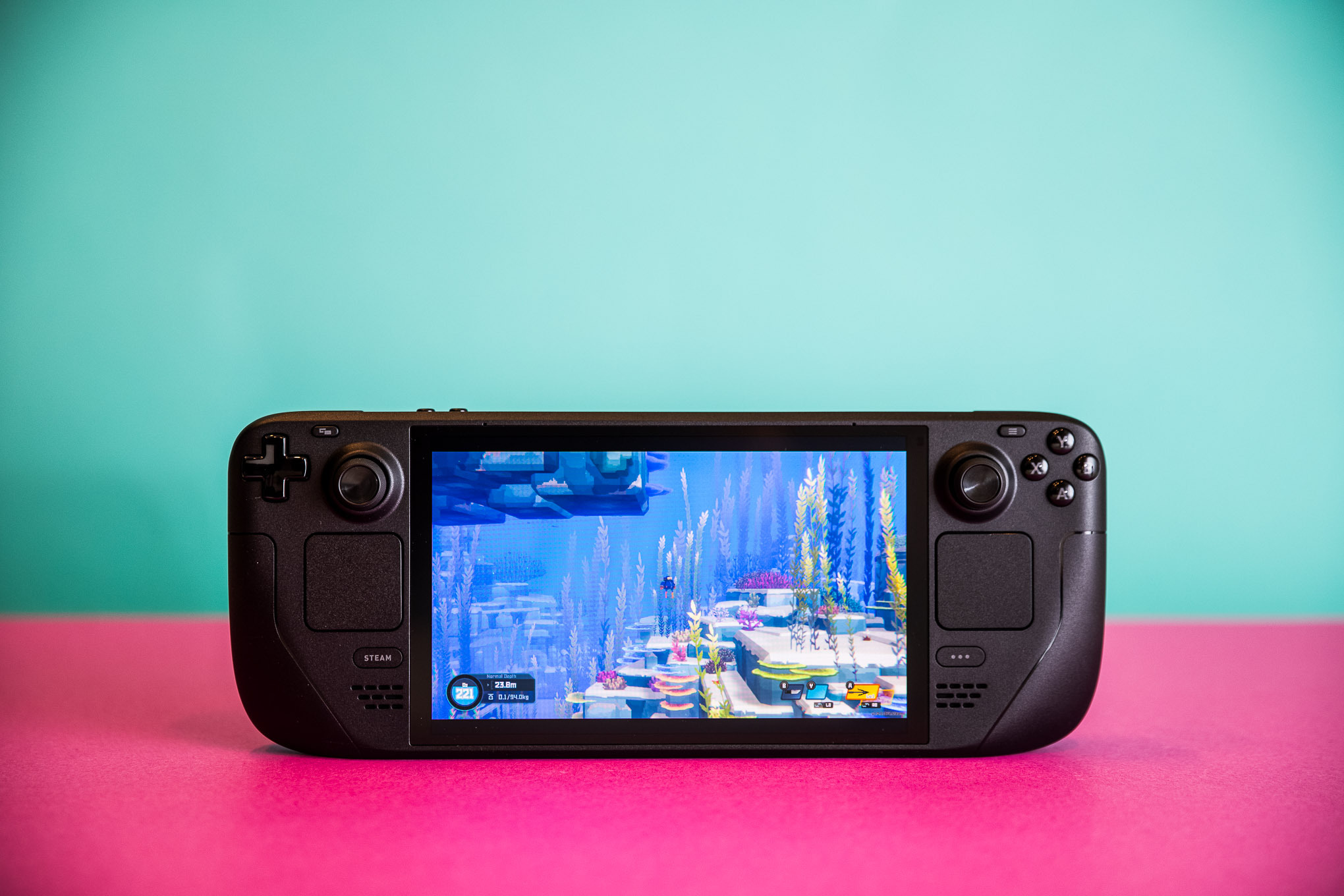 Photographs of the Steam Deck OLED, and of its hard zip-up case. Each photo is taken with the handheld sitting on a hot pink sheet of thick paper.