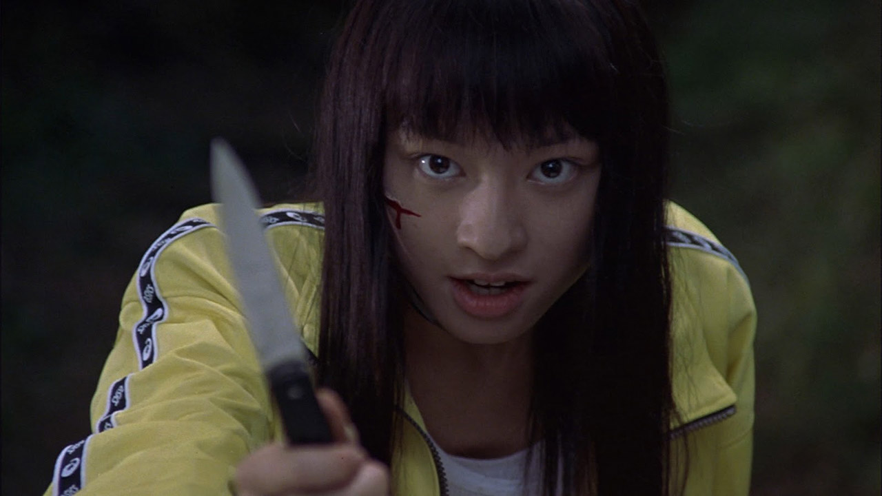 Chiaki Kuriyama as Takako Chigusa in a yellow tracksuit brandishing a knife in Battle Royale.