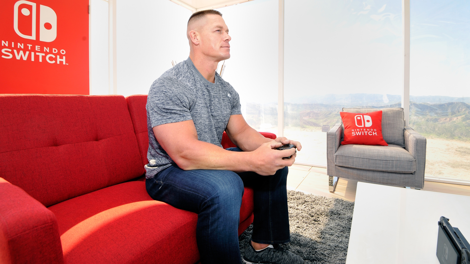 John Cena sits in a Nintendo Switch-themed room playing a Nintendo Switch